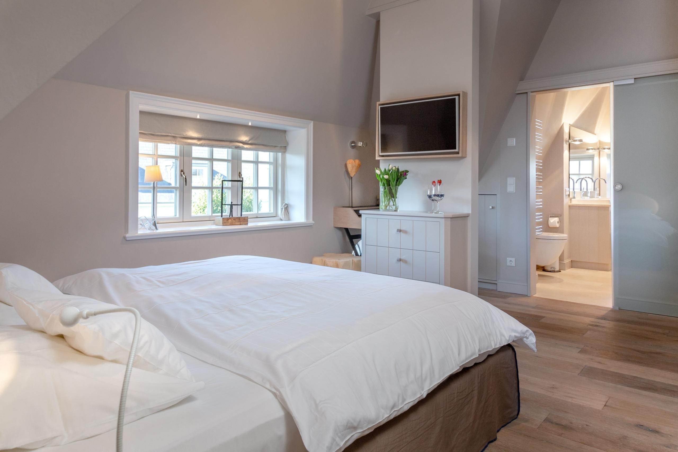 Doppelbett mit Fernseher und Badezimmer in Ferienwohnung auf Sylt