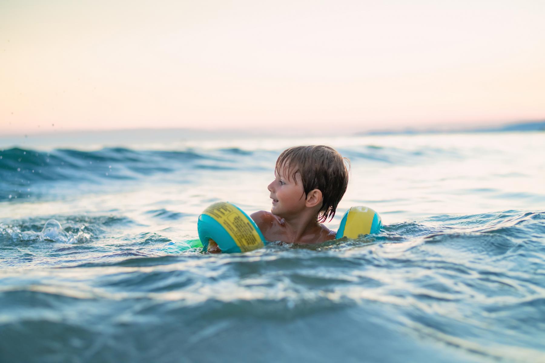 klein Junge mit Schwimmflügeln im Meer